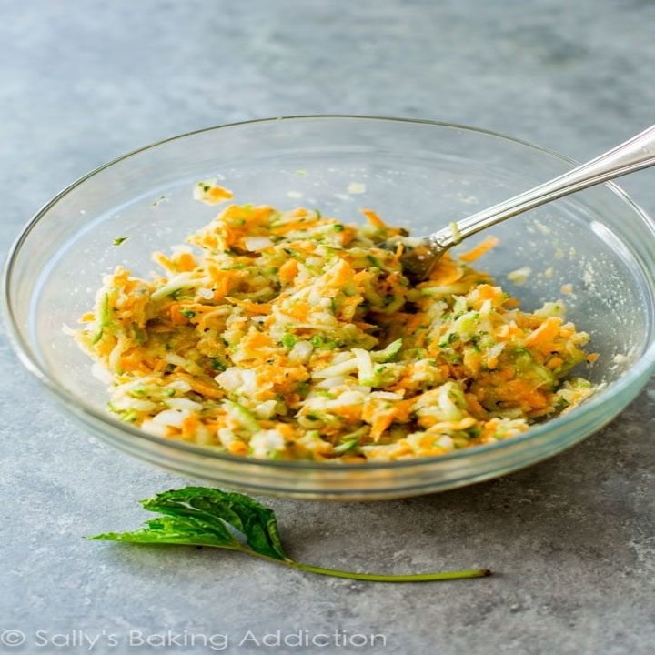 Shredded zucchini and sweet potato in a bowl, mixed with beaten eggs.
