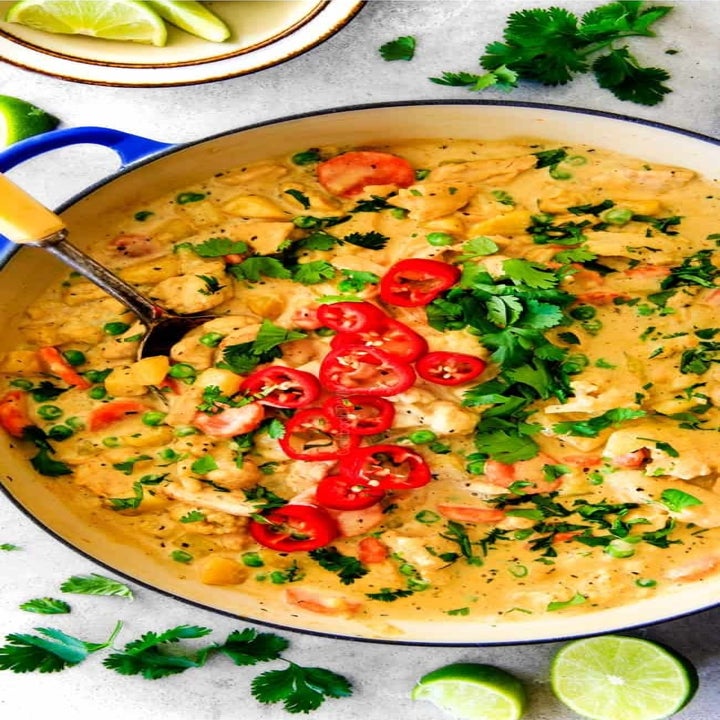 A big pot of yellow chicken curry with vegetables and fresh herbs.