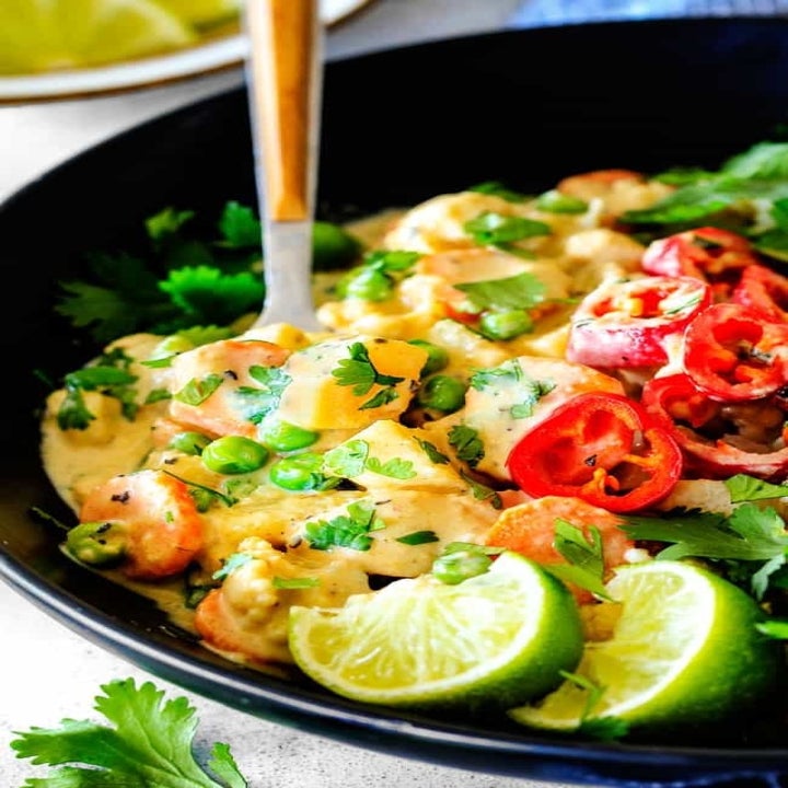 A bowl of chicken curry with peppers and limes.