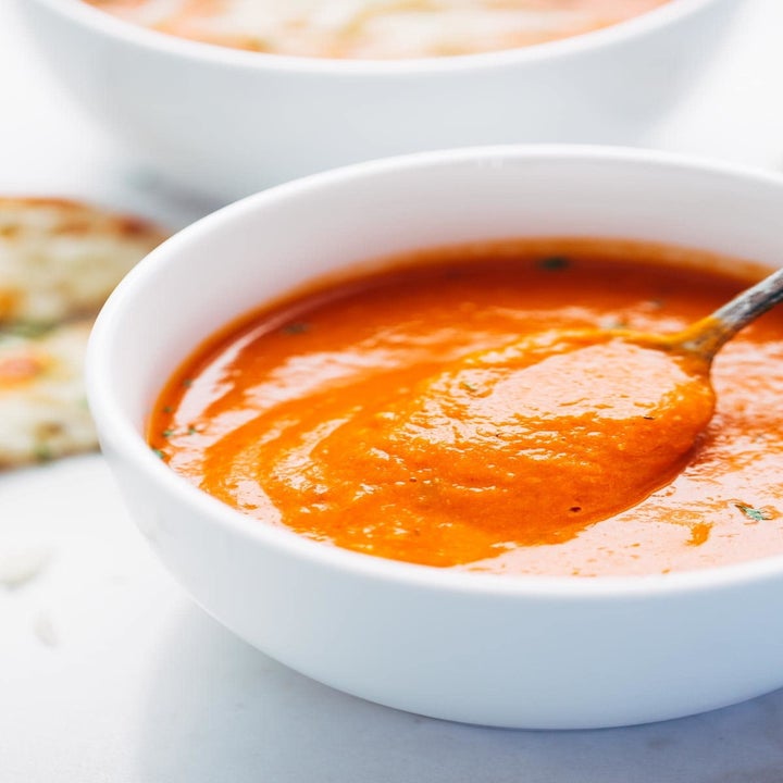 A spoon dipping into a bowl of creamy tomato soup.
