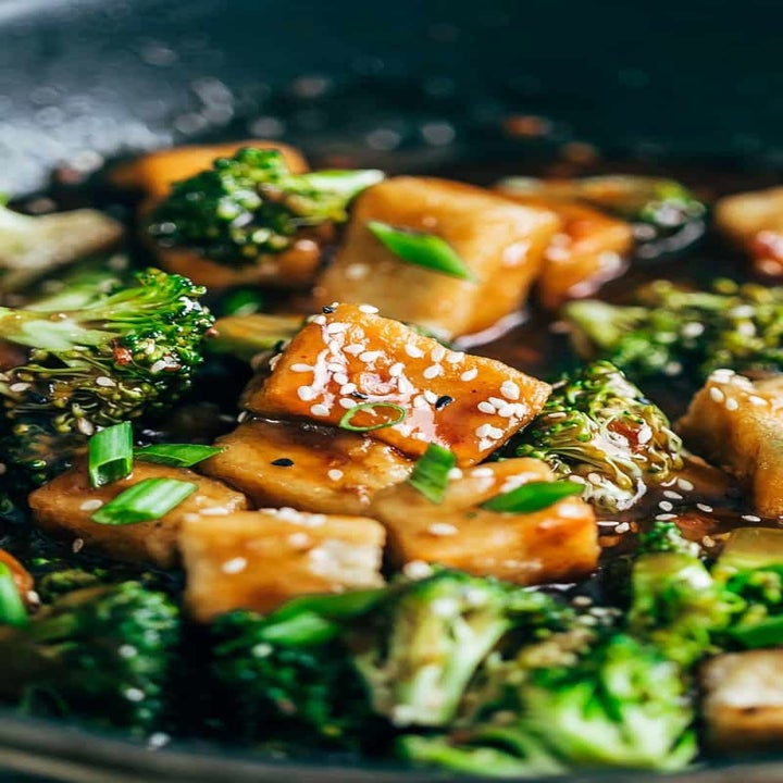 Cubes of tofu and broccoli in an Asian sauce with sesame seeds in a pan.