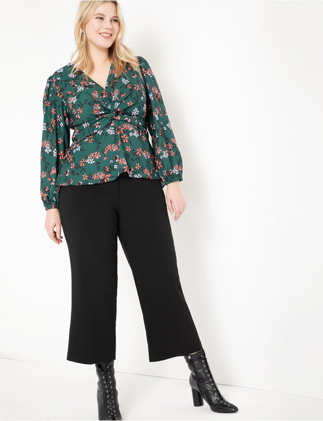 A model wearing the dark green floral blouse, which has small pink and white flowers and black leaves on it 