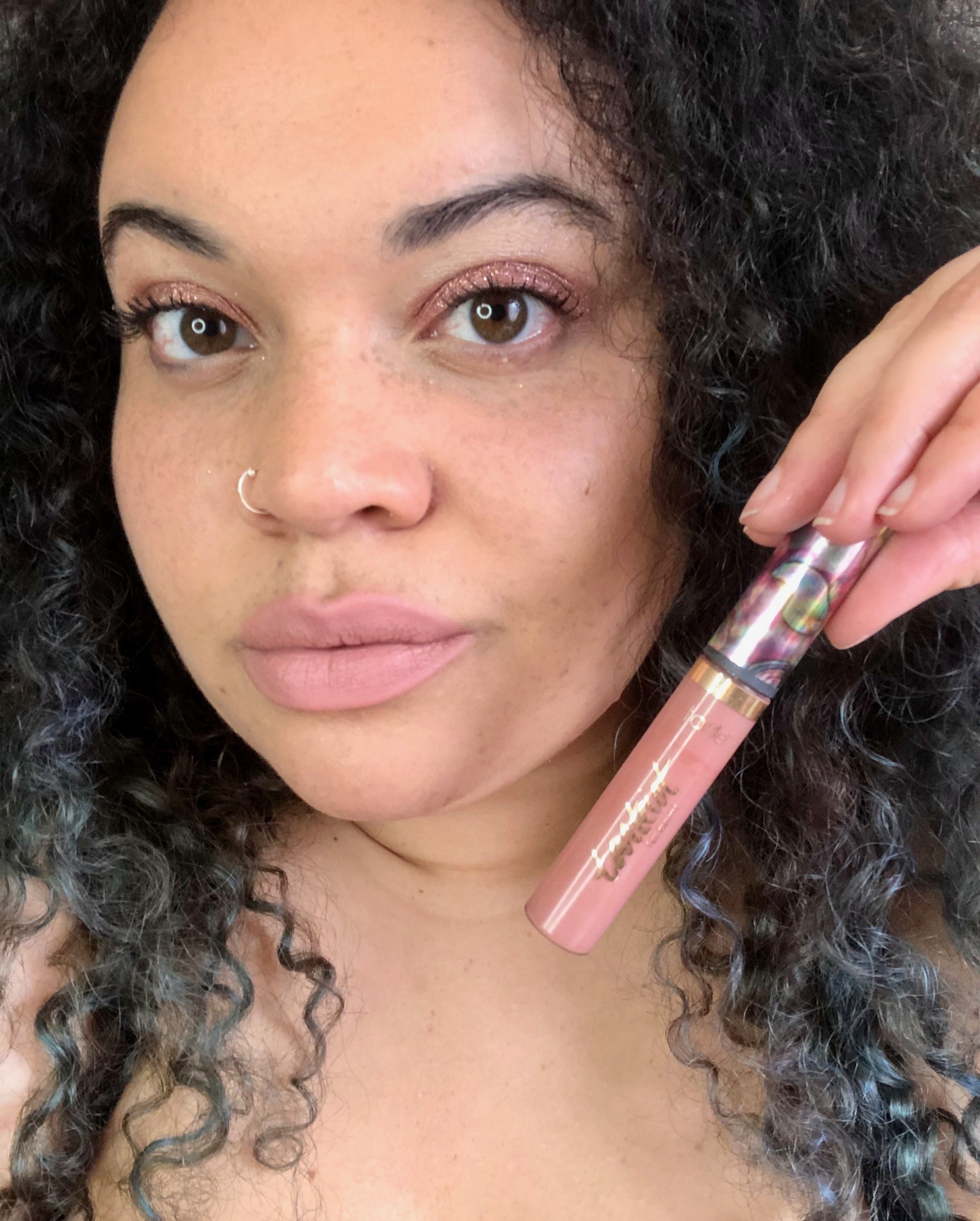 BuzzFeed Shopping reviewer holding the lip paint in light pink with a matching lip 