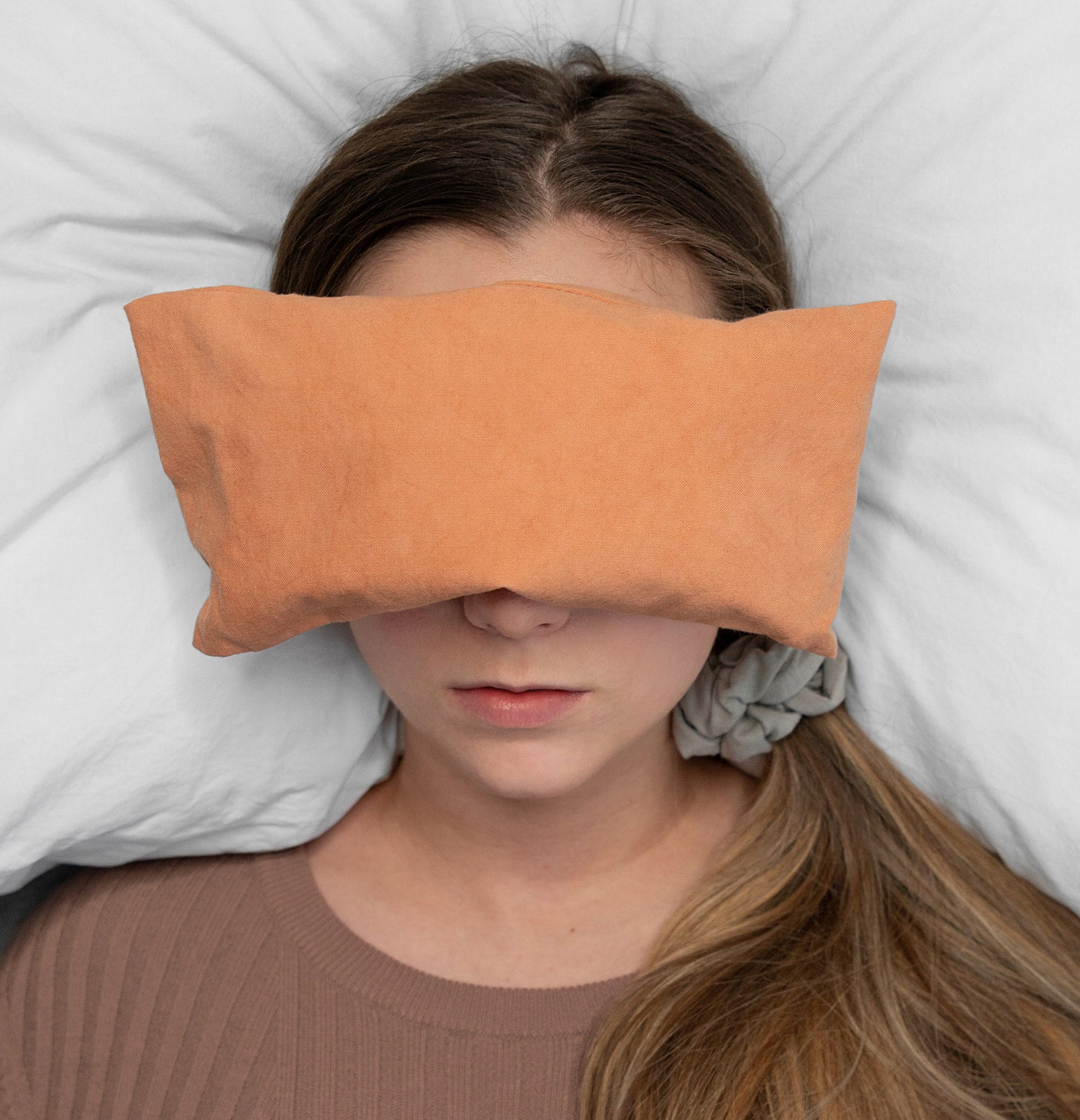 A person lying on a bed with a rectangular bean bag over their eyes