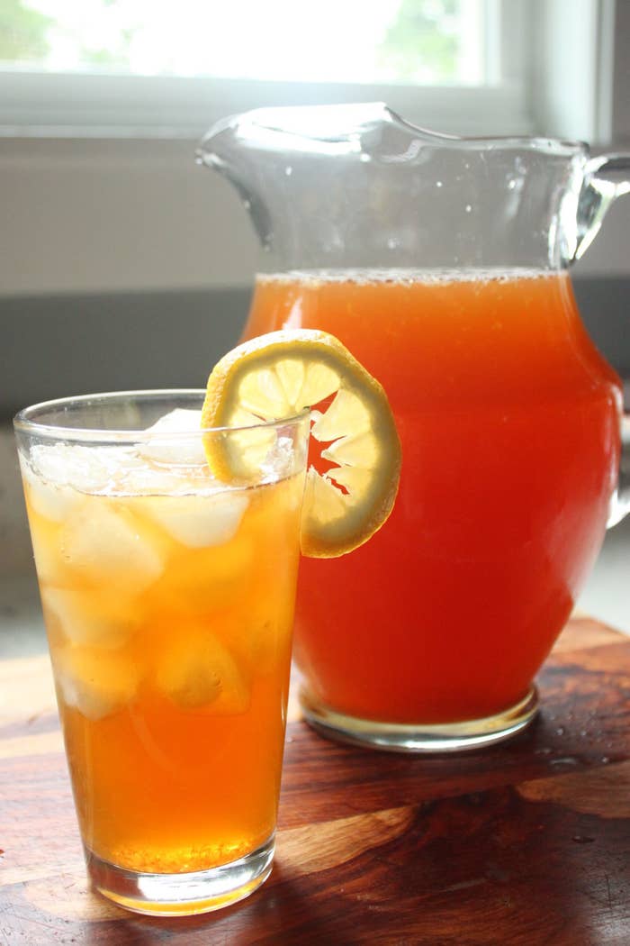 Black tea lemonade in a tall glass garnished with a lemon slice and a pitcher of the drink in the background