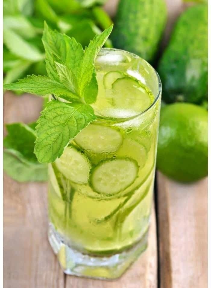 The green-hued refresher in a glass with cucumber and lime slices inside and a mint leaf garnish