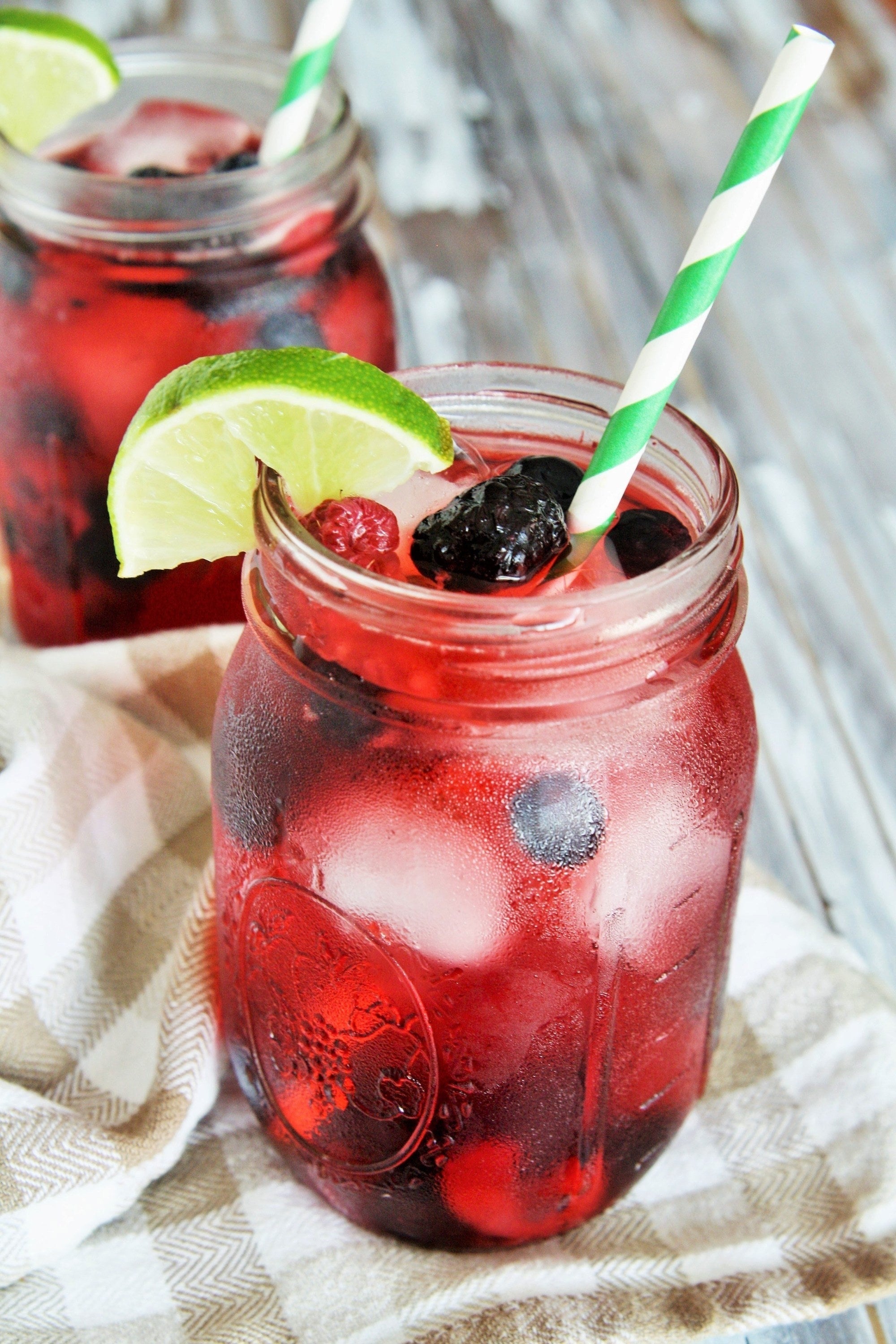 A bright red drink filled with various berries inside a glass mason jar garnished with a lime wedge