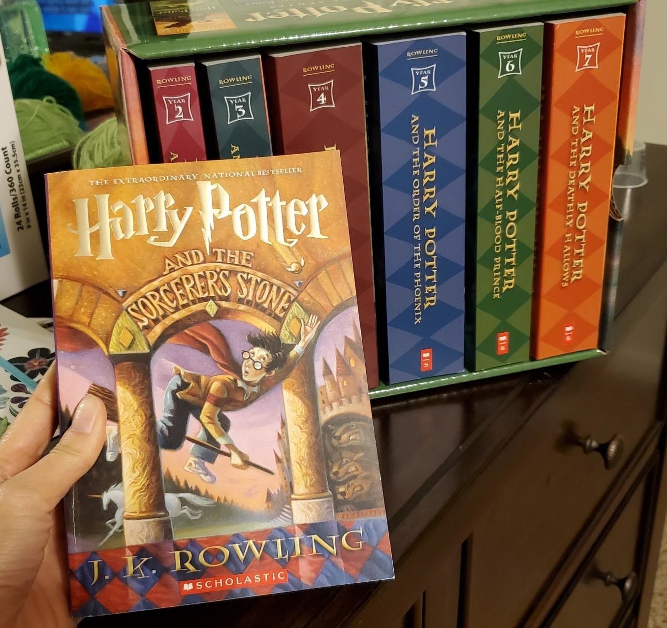 reviewer holding first harry potter book in front of the paperback box set in its decorative cardboard case