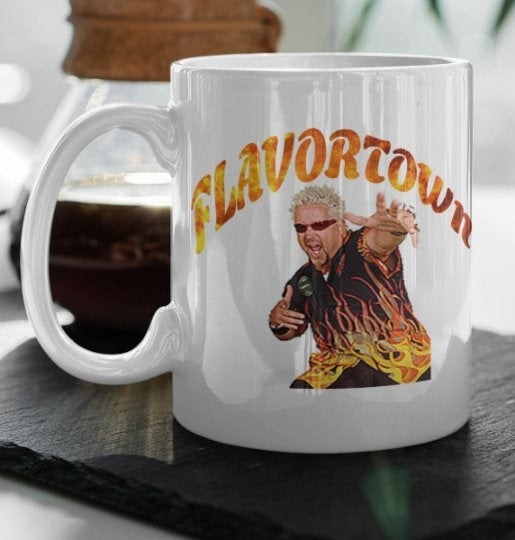 a white coffee mug with guy fieri and the flaming words &quot;flavortown&quot; on it
