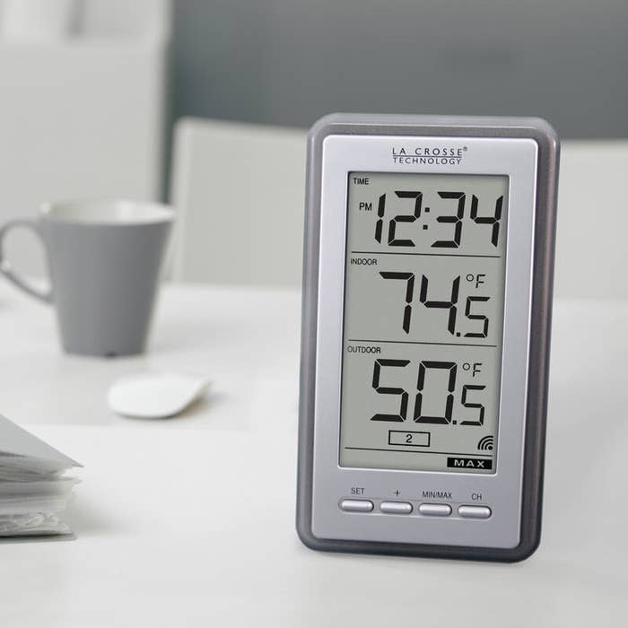 A rectangular, palm-sized screen digitally displays the time, indoor temperature, and outdoor temperature