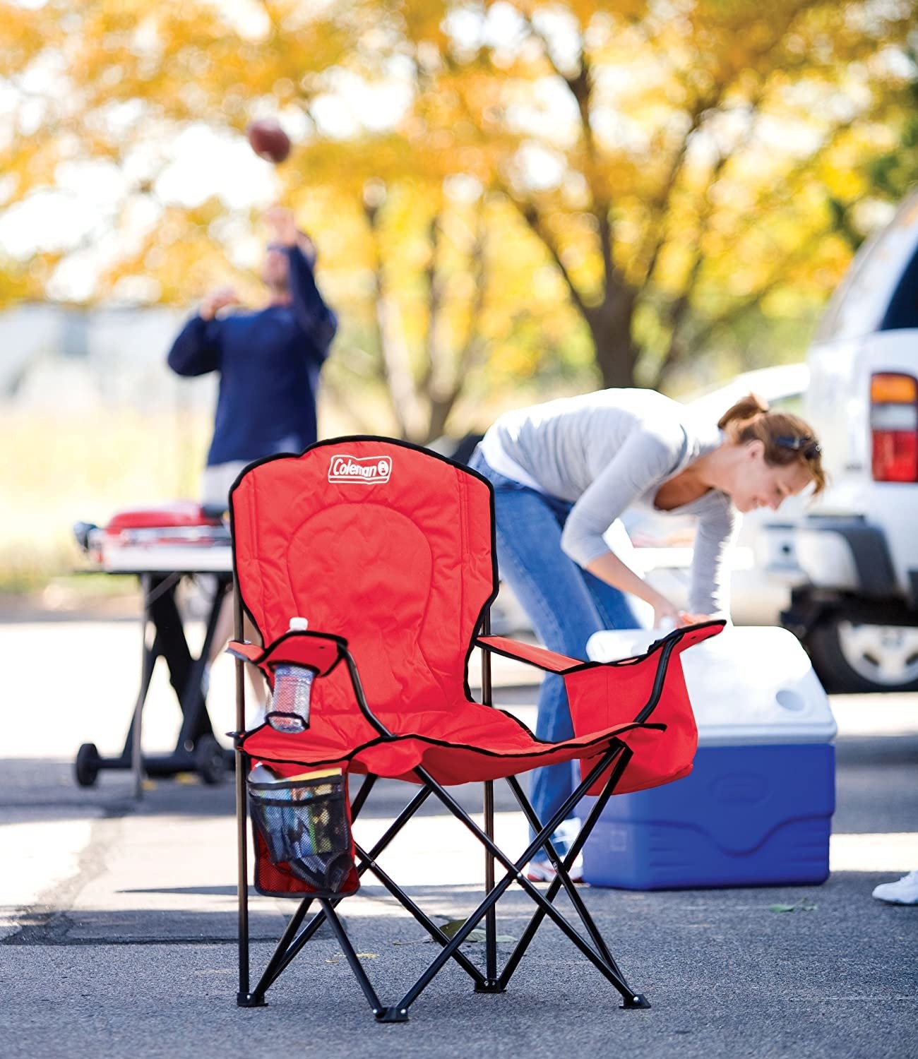 An open red Coleman chair with beverage holder, coolers, and side pouch in full use