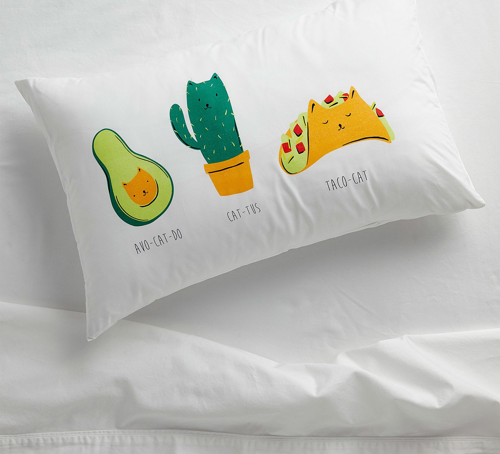 A pillowcase with three illustrations of a cat as an avocado, cactus and taco