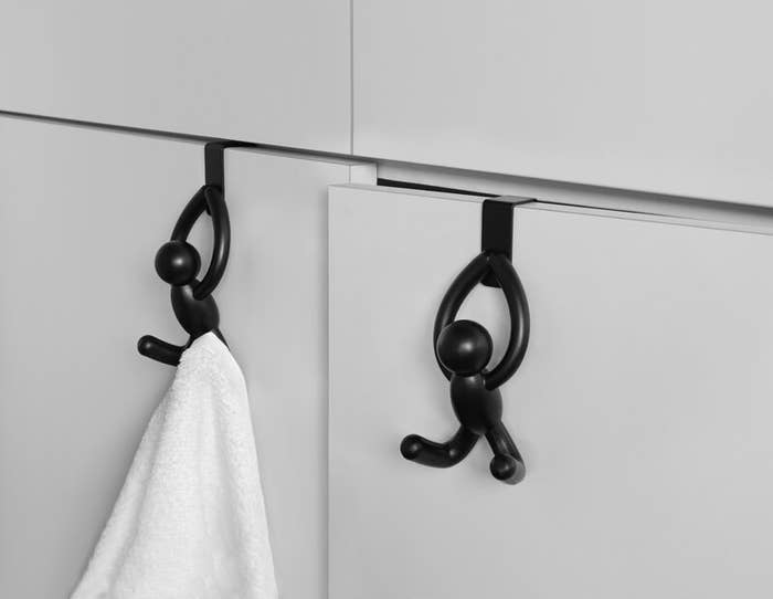 Two over-the-door hooks shaped like stick figures with their legs extended out like a hook hanging over a cabinet door