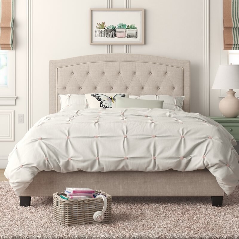A made-bed resting on an upholstered platform with a matching rounded and tufted headboard