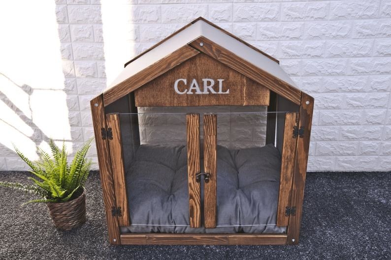 a chic looking dog house with clear double doors that open outwards and their name personalized on the front above the doors