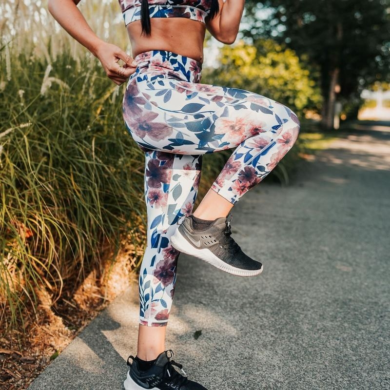 Model wearing 7/8 leggings in white with a green, purple, and orange floral pattern