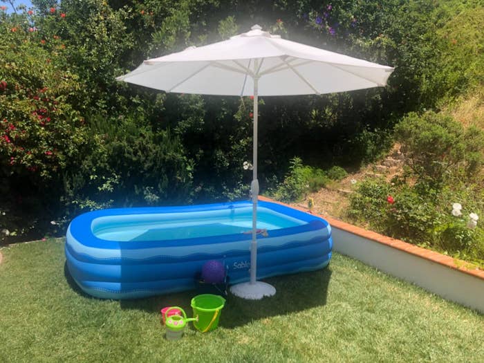 A rectangular inflatable pool in a backyard under an umbrella