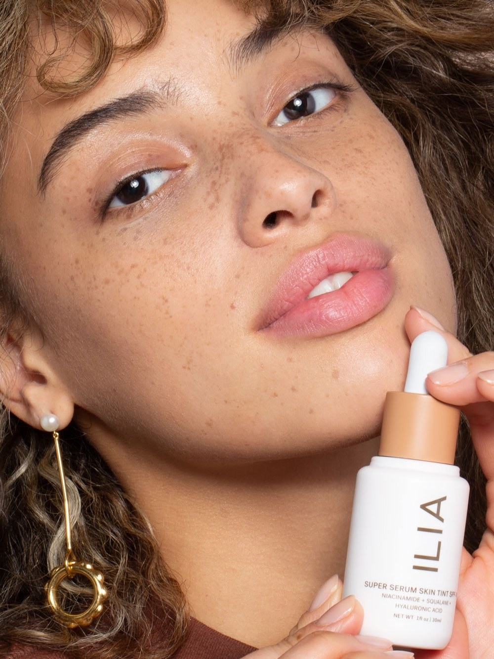A model holding the skin tint bottle with a dropper top close to her face