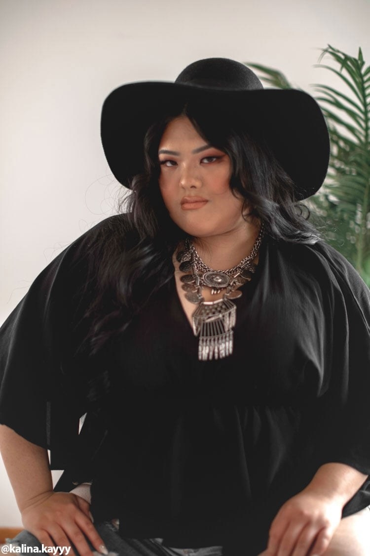 model wearing top in black with silver necklace and black hat