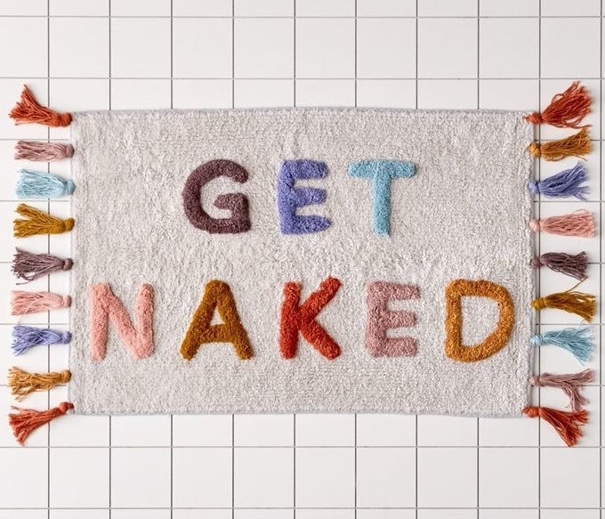 A colorful bath mat with the words &quot;Get Naked&quot; and tassels on two sides 