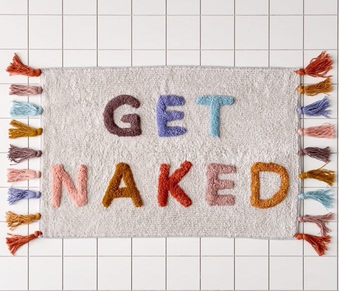 A colorful bath mat with the words &quot;Get Naked&quot; and tassels on two sides 