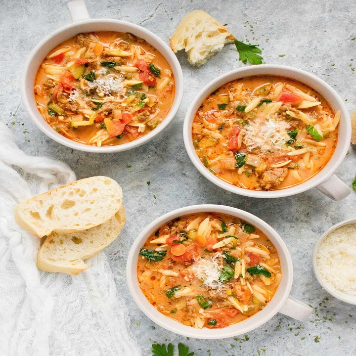 Three bowls of Italian sausage orzo soup with crusty bread on the side.