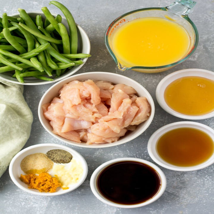 Ingredients for orange chicken in little bowls: Orange juice, raw chicken, sesame oil, and spices..