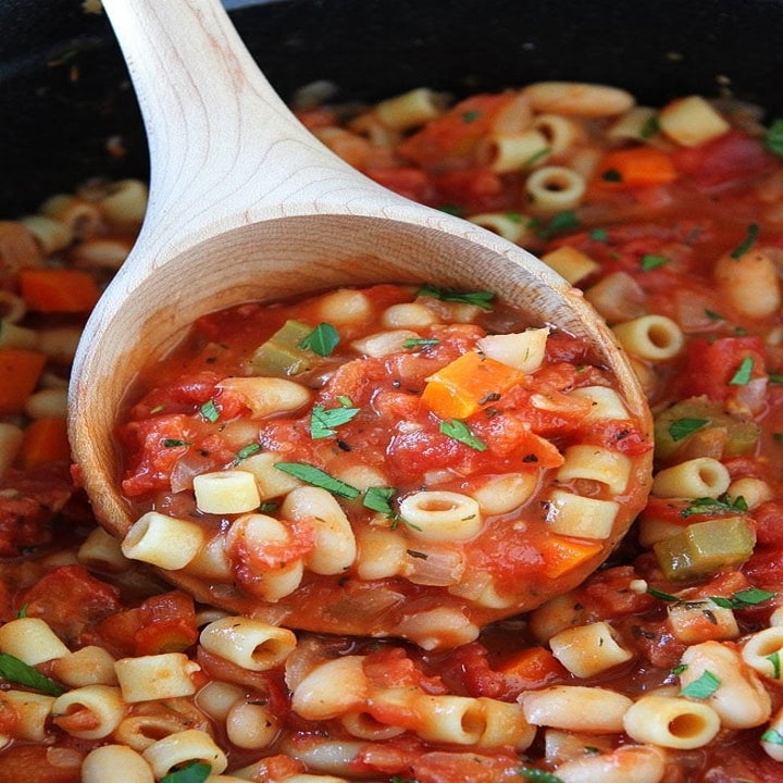 A close-up of pasta fagioli soup on a wooden spoon.