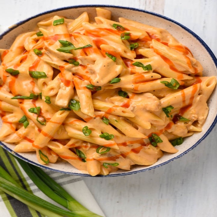 A big bowl of buffalo chicken mac 'n' cheese topped with fresh herbs and buffalo sauce.