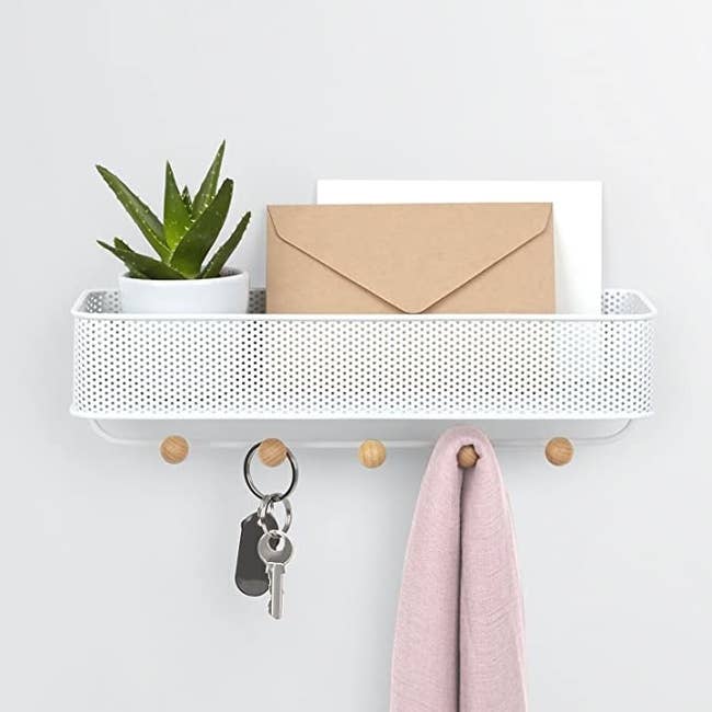 Mail organizer with perforated metal bin and five hooks with wooden knobs under it on a wall