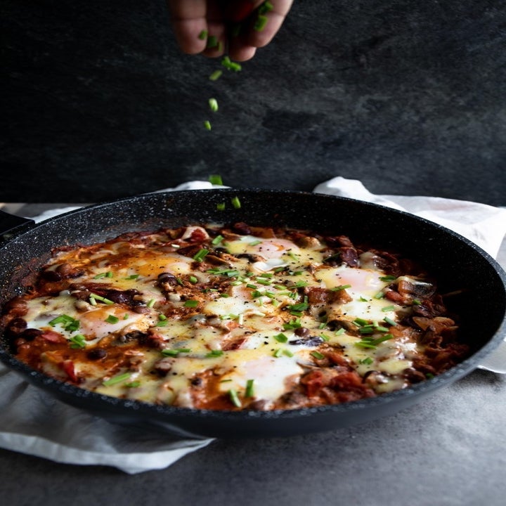 Sprinkling herbs on baked eggs and beans with stewed tomatoes in a skillet.