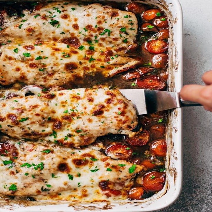A baking dish full of cooked chicken topped with golden brown melted cheese in a tomato and balsamic sauce.