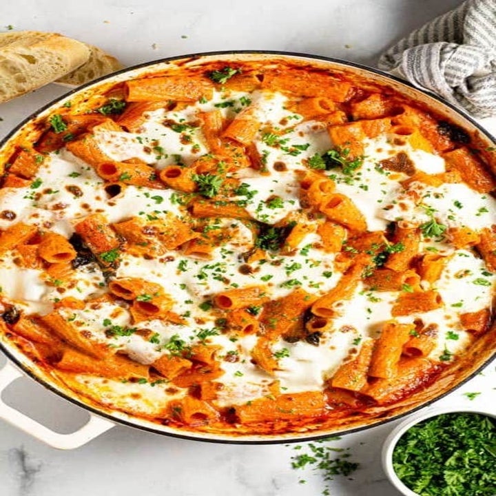 A pot of baked pasta in marinara sauce with melted cheese and fresh chopped herbs.