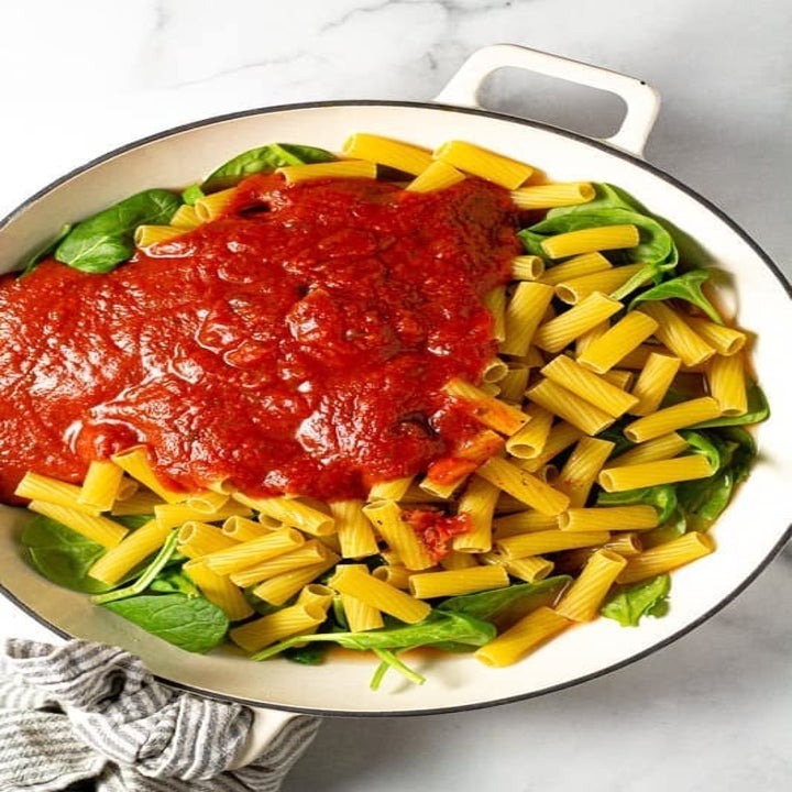 A big pot of uncooked pasta, spinach, and marinara sauce.