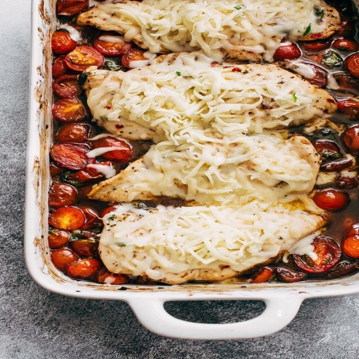 Chicken breasts covered with shredded cheese in a baking dish surrounded by cherry tomatoes in a balsamic sauce.