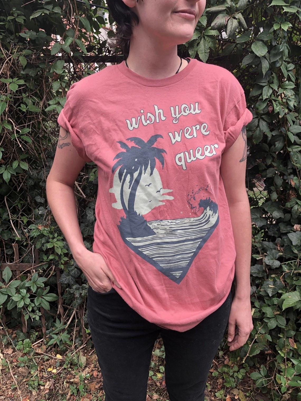 model wearing shirt with beach design and text &quot;wish you were queer&quot; 