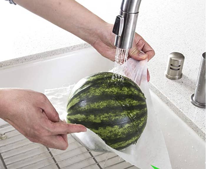 A person washing a mini watermelon suspended on a bamboo paper towel, demonstrating its durability 