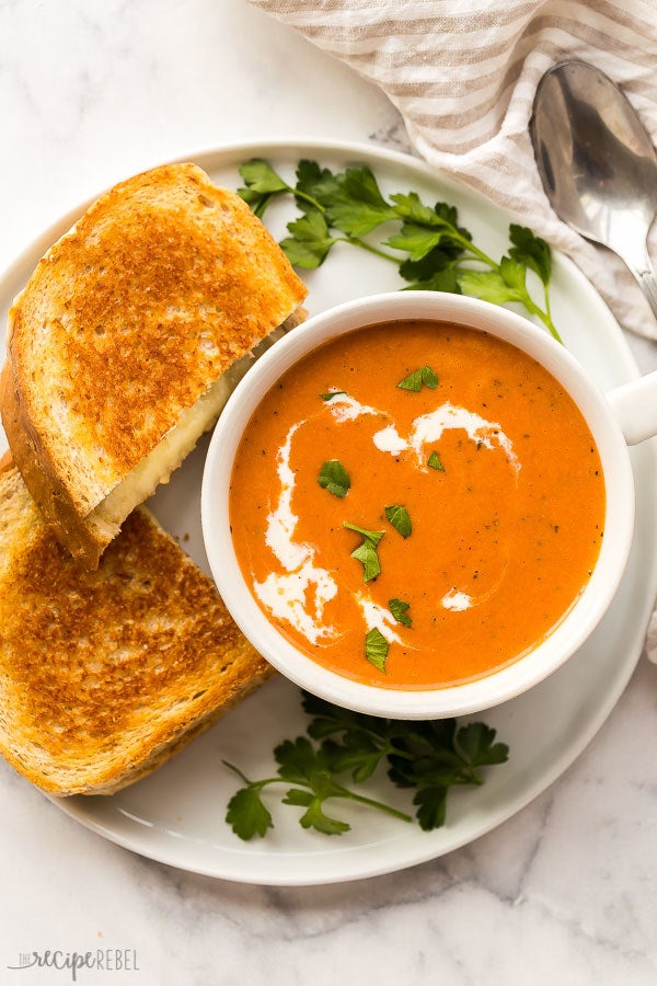 A bowl of creamy tomato soup with two halves of grilled cheese on the side.