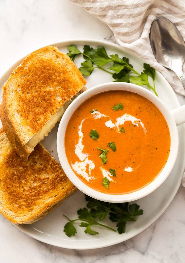 A bowl of creamy tomato soup with two halves of grilled cheese on the side.
