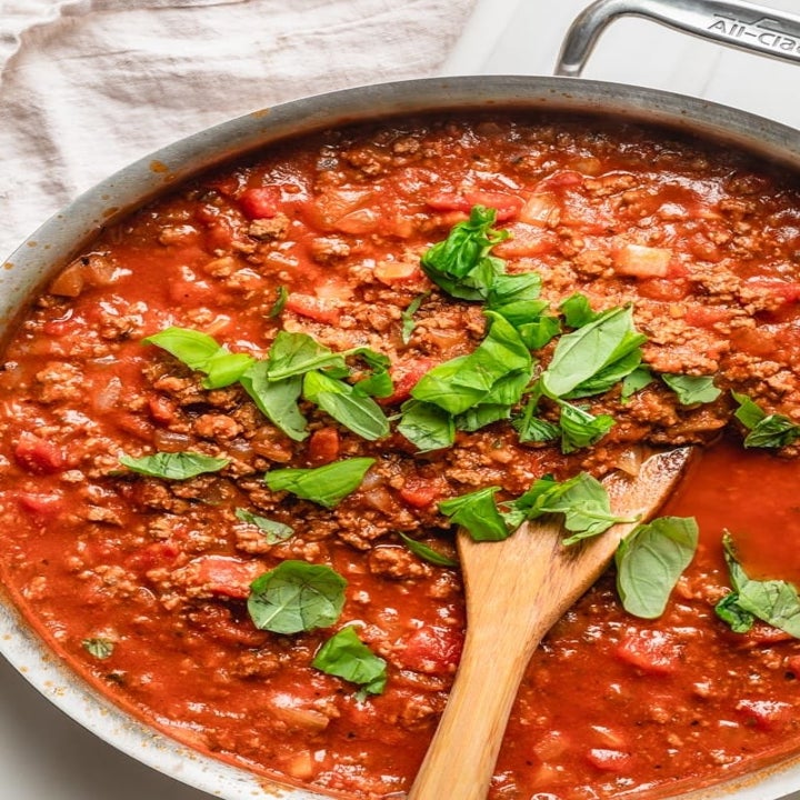 A big sauce pan full of diced tomatoes, ground beef, and fresh herbs for Bolognese sauce.