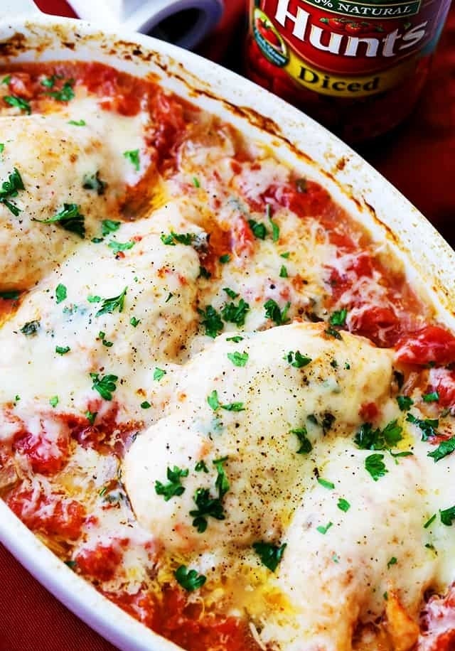 A baking dish full of cheesy baked chicken in tomato sauce with fresh herbs.