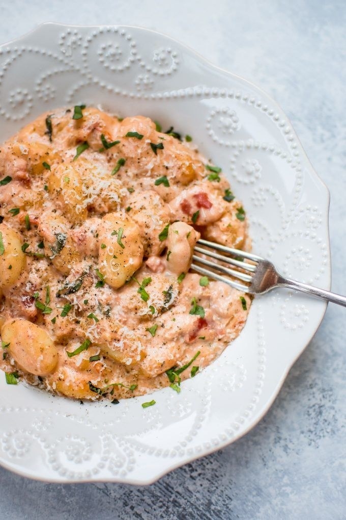 A bowl of gnocchi in creamy tomato sauce with fresh herbs.