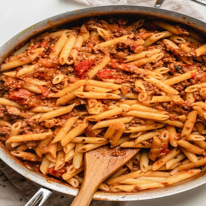 Pasta mixed into Bolognese sauce in a pan.