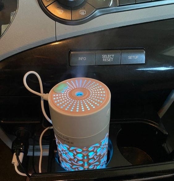 Reviewer using the mini car diffuser in their car&#x27;s cup holder