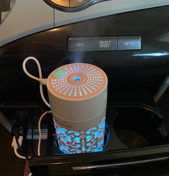 Reviewer using the mini car diffuser in their car's cup holder