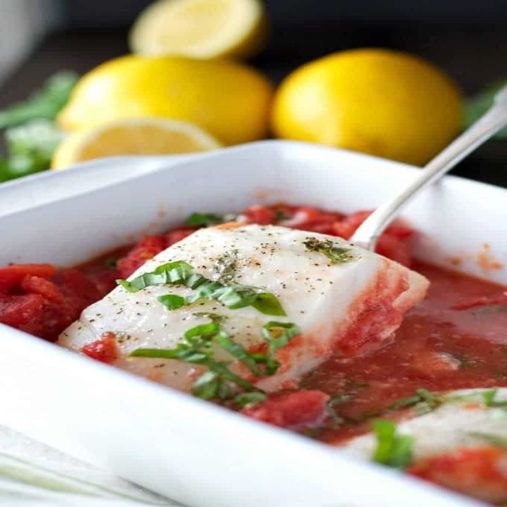A piece of fish being spooned from a bed of tomato sauce.