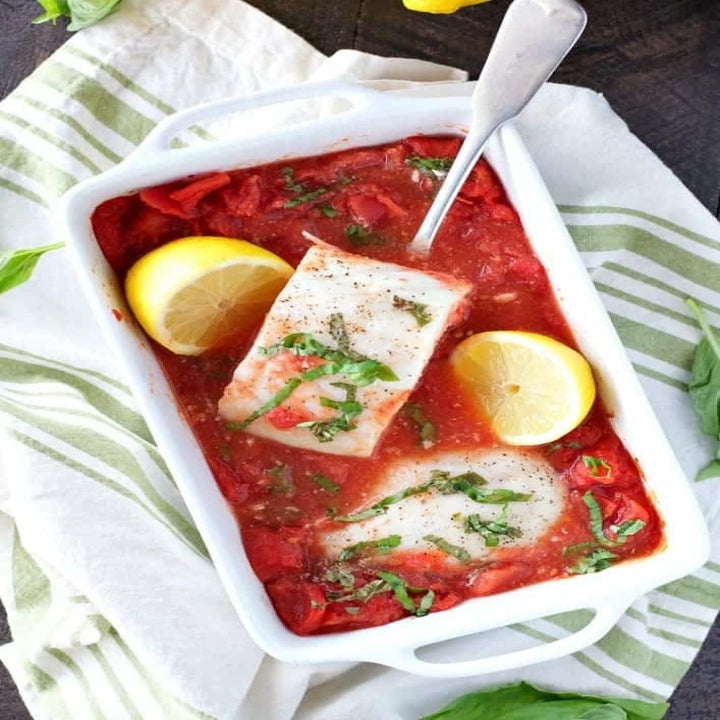 A baking dish with two pieces of fish in tomato sauce.