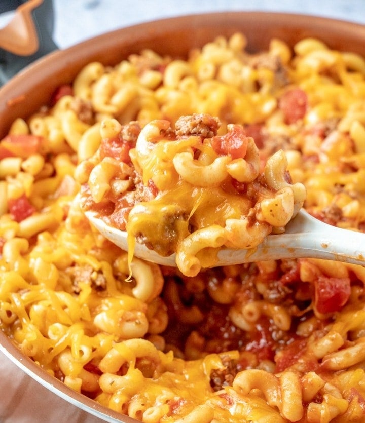 A spoon digging into a big bowl of mac &#x27;n&#x27; cheese with ground beef.