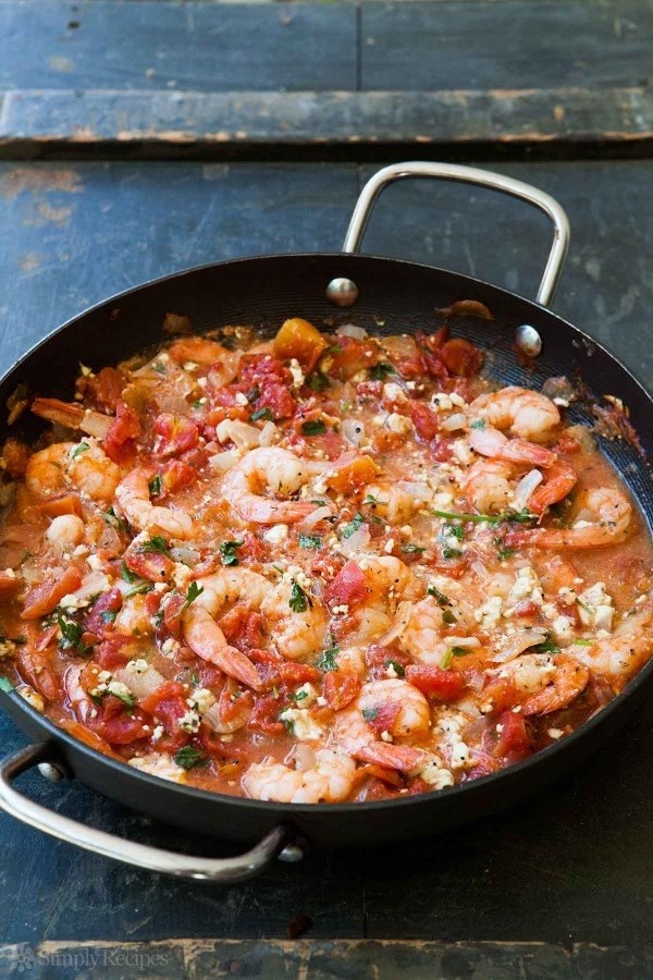 A skillet with shrimp baked in a sauce made of diced tomatoes and feta cheese with some fresh herbs.