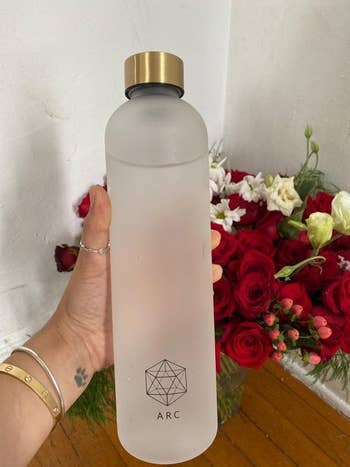 Same hand holding the water bottle to show its back with a geometric design at the bottom